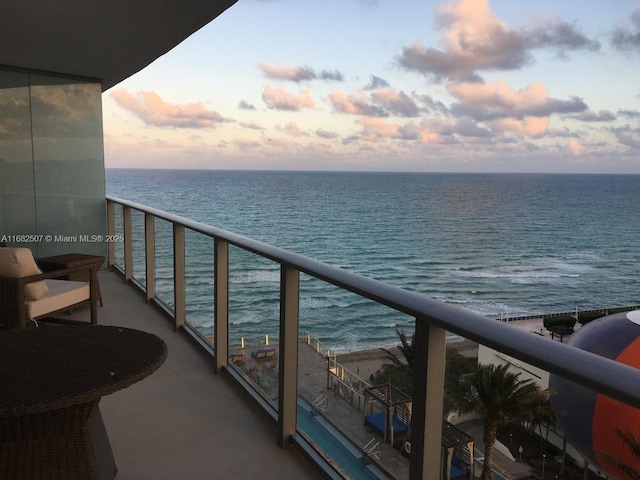 balcony at dusk featuring a water view