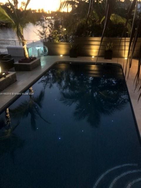 pool at dusk featuring a fire pit, a patio area, and a jacuzzi