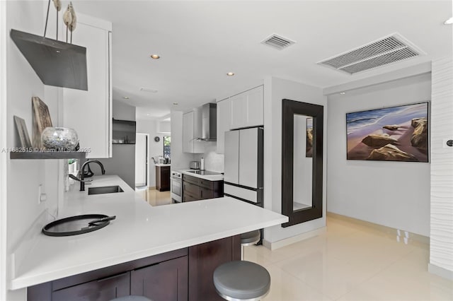 kitchen with kitchen peninsula, wall chimney exhaust hood, sink, white cabinets, and oven