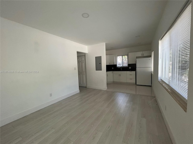 unfurnished living room with sink, electric panel, and light hardwood / wood-style floors