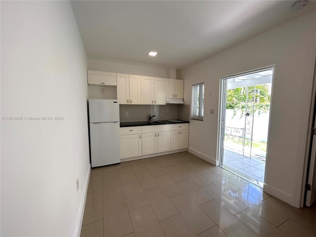 kitchen with sink, light tile patterned floors, white refrigerator, and white cabinets