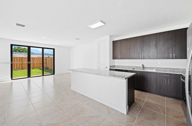 kitchen featuring dark brown cabinets, light tile patterned floors, light stone countertops, sink, and a center island