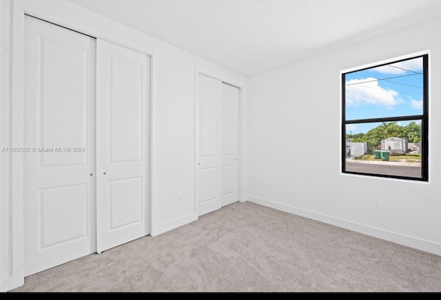 unfurnished bedroom with multiple closets and light colored carpet