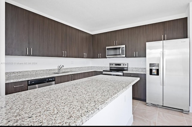 kitchen featuring sink, light stone countertops, dark brown cabinetry, and stainless steel appliances