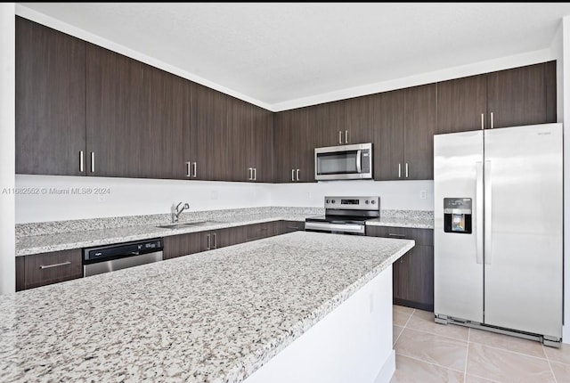 kitchen featuring dark brown cabinetry, light stone countertops, stainless steel appliances, and sink