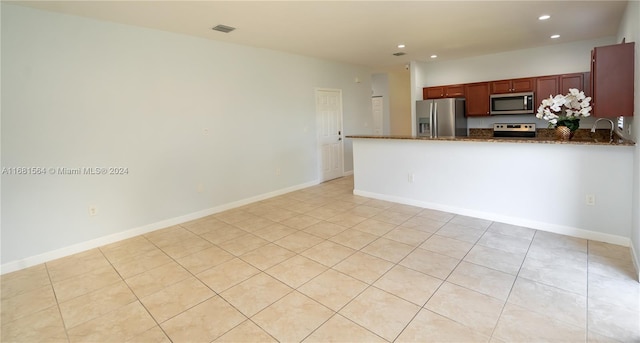 kitchen featuring kitchen peninsula, stainless steel appliances, light tile patterned floors, and dark stone counters