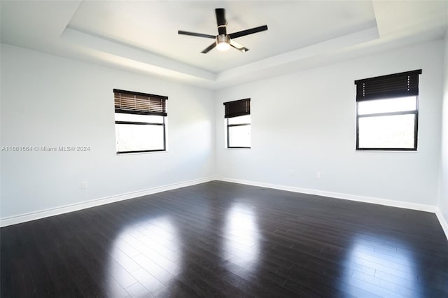 empty room with ceiling fan, a tray ceiling, and dark hardwood / wood-style flooring