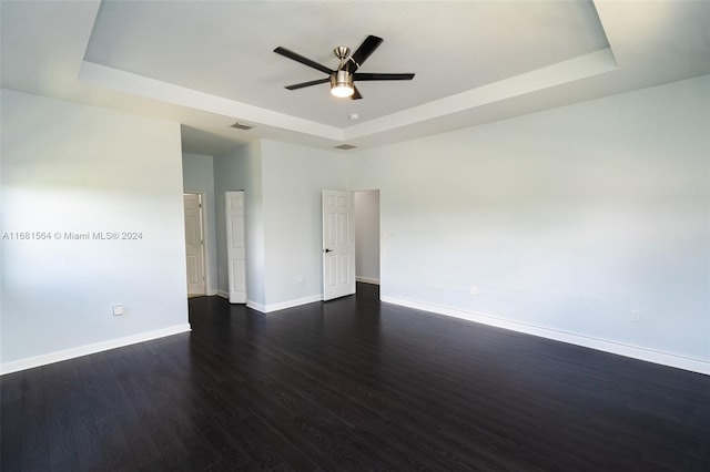 empty room with ceiling fan, a tray ceiling, and dark hardwood / wood-style flooring