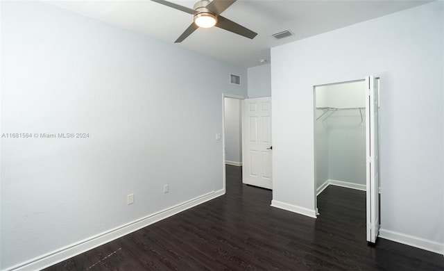 unfurnished bedroom with a closet, ceiling fan, a walk in closet, and dark hardwood / wood-style floors