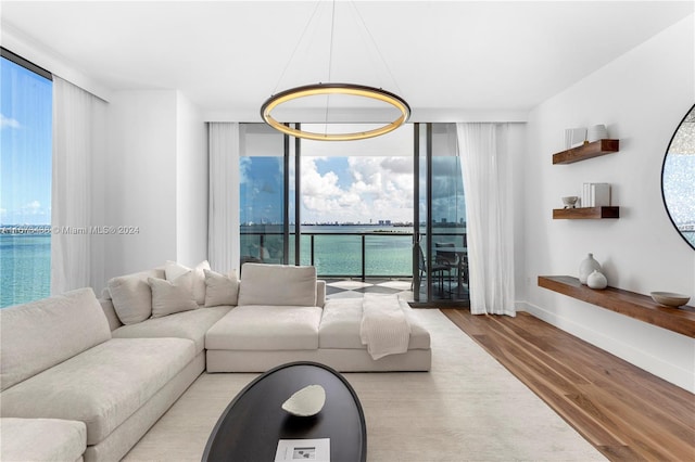 living area featuring a water view, baseboards, floor to ceiling windows, and wood finished floors