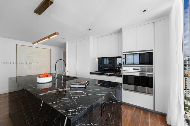 kitchen featuring a center island with sink, stainless steel oven, white cabinetry, dark stone countertops, and dark wood-type flooring