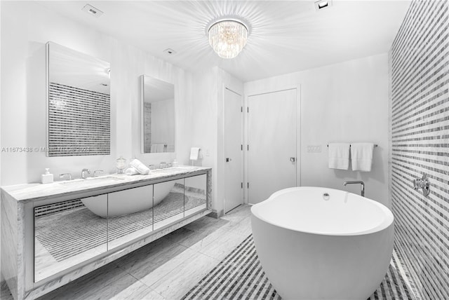 bathroom featuring an inviting chandelier, double vanity, visible vents, a freestanding bath, and a sink