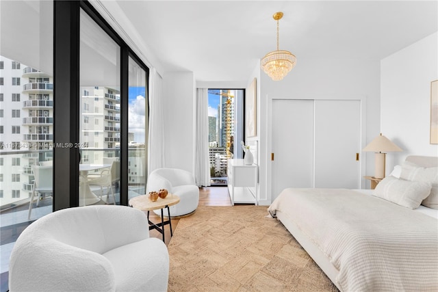 bedroom with expansive windows, access to outside, an inviting chandelier, light hardwood / wood-style floors, and a closet