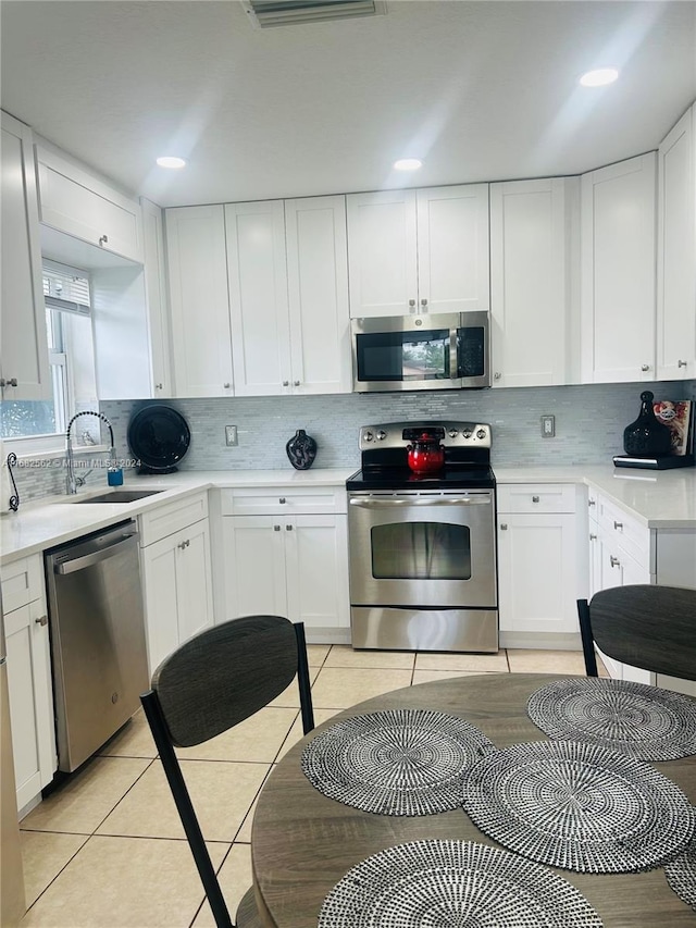 kitchen featuring decorative backsplash, white cabinets, stainless steel appliances, and light tile patterned floors