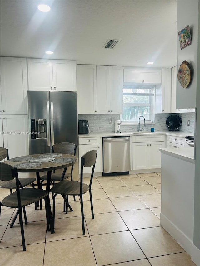 kitchen featuring decorative backsplash, white cabinetry, stainless steel appliances, and light tile patterned floors