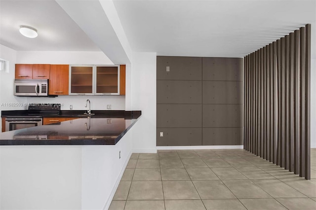 kitchen with kitchen peninsula, stainless steel appliances, dark stone counters, sink, and light tile patterned flooring