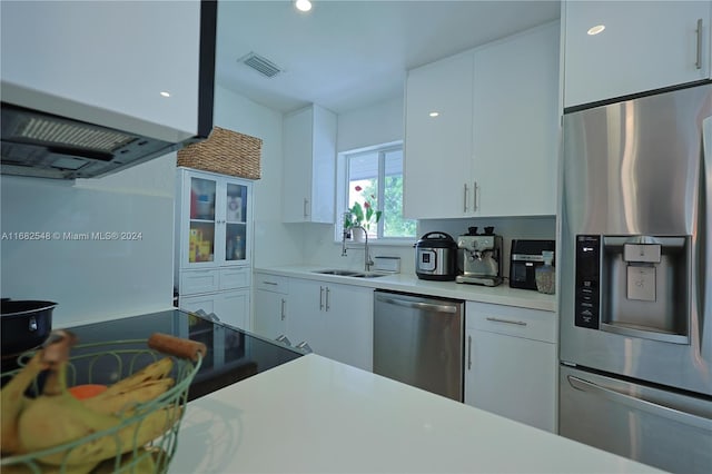 kitchen featuring appliances with stainless steel finishes, white cabinets, sink, and range hood