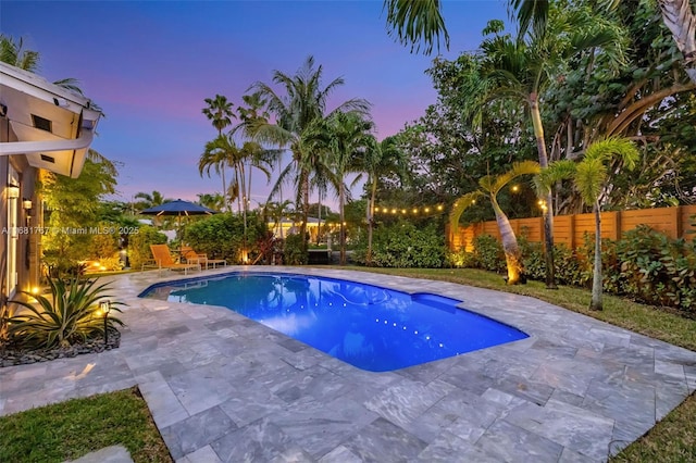 pool at dusk featuring a patio area, a fenced backyard, and a fenced in pool