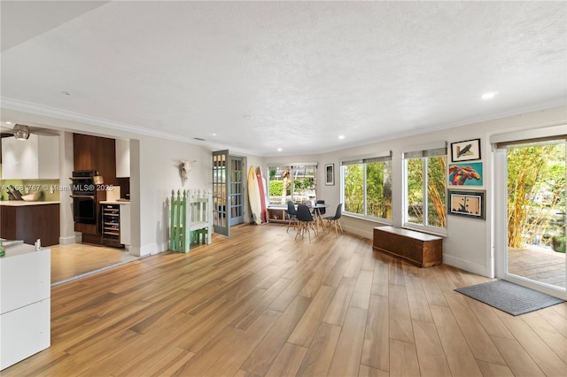 interior space with light wood-type flooring, crown molding, a textured ceiling, and wine cooler