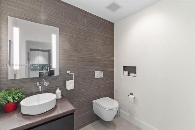 bathroom with toilet, vanity, baseboards, visible vents, and tile walls