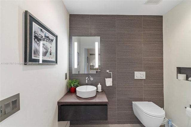 bathroom featuring visible vents, vanity, toilet, and tile walls