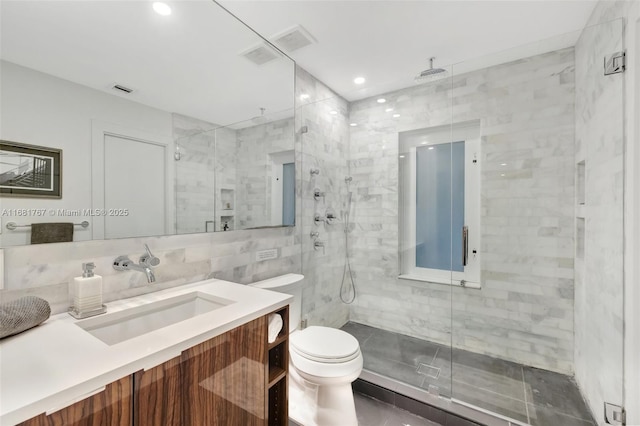 full bathroom with a stall shower, toilet, tile walls, and vanity