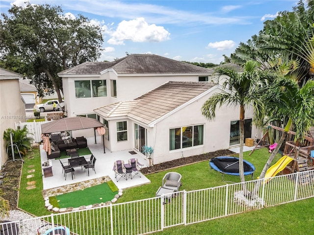 rear view of property featuring a patio area, an outdoor living space, a yard, and a trampoline