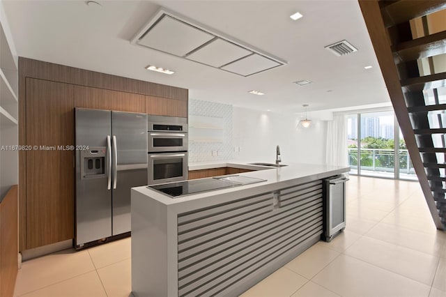 kitchen featuring decorative backsplash, hanging light fixtures, stainless steel appliances, a center island with sink, and light tile patterned floors