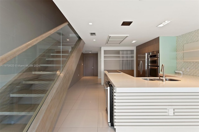 kitchen featuring double oven, light tile patterned flooring, sink, and kitchen peninsula