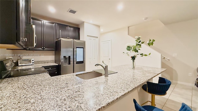 kitchen with kitchen peninsula, a kitchen bar, stainless steel appliances, and light stone countertops