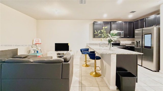 kitchen featuring a kitchen bar, kitchen peninsula, light stone countertops, stainless steel appliances, and light tile patterned floors