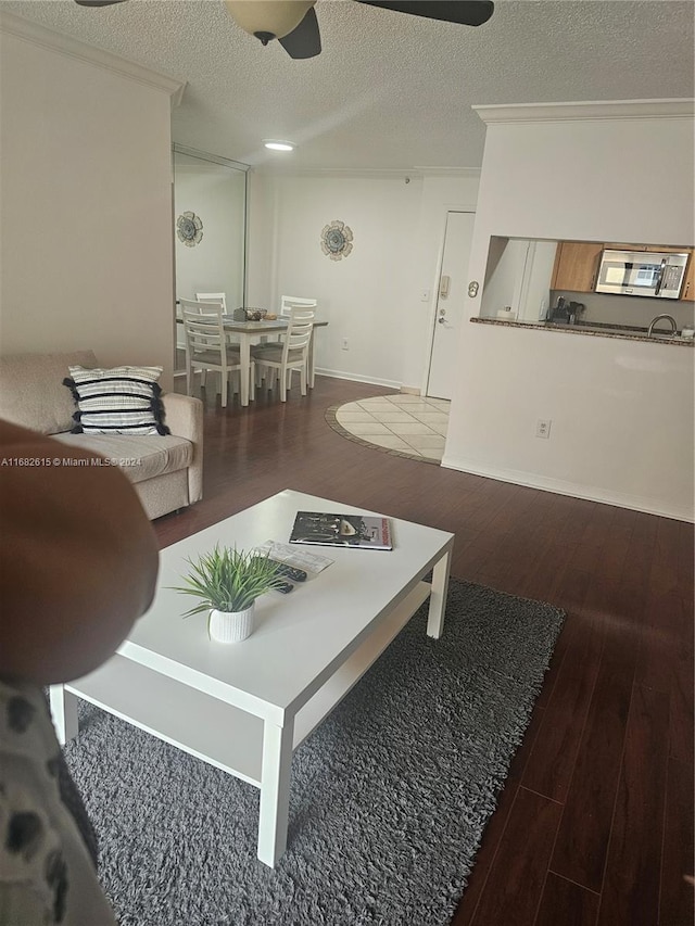 living room with crown molding, dark hardwood / wood-style floors, a textured ceiling, and ceiling fan