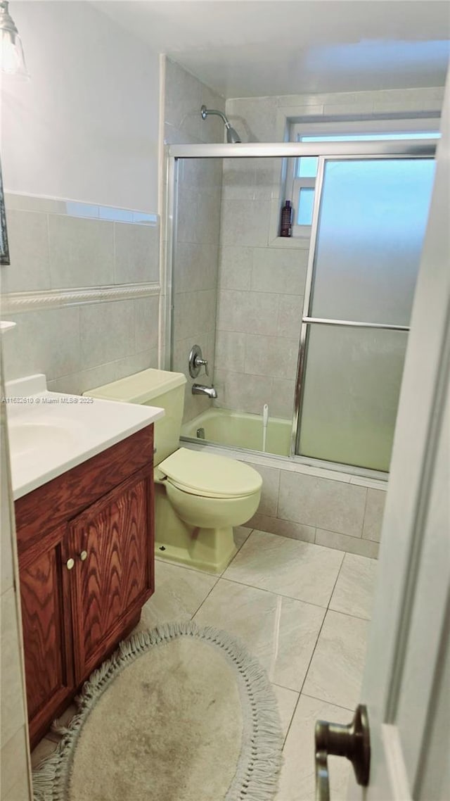 full bathroom featuring enclosed tub / shower combo, tile patterned floors, toilet, vanity, and tile walls