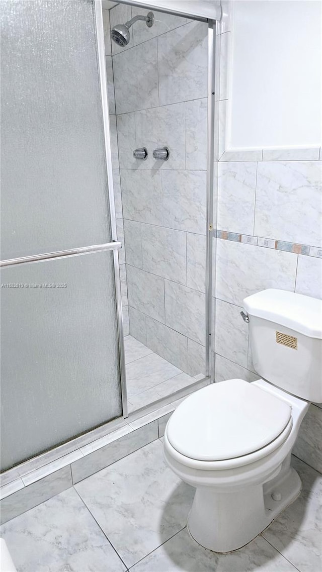 bathroom featuring a shower with shower door, tile walls, and toilet