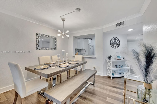 dining area featuring ornamental molding, light hardwood / wood-style flooring, a notable chandelier, and a textured ceiling