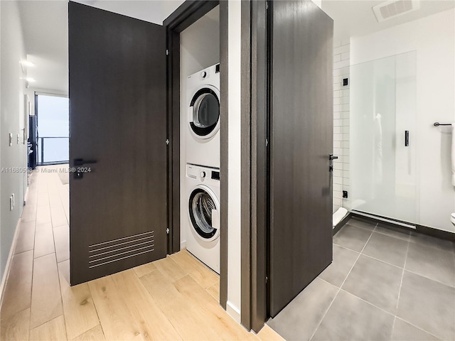 laundry room with light wood-type flooring and stacked washer and clothes dryer