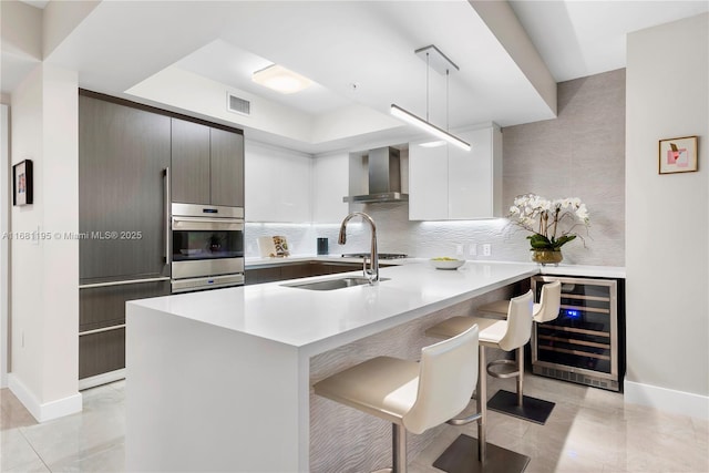 kitchen with wine cooler, oven, visible vents, wall chimney range hood, and a kitchen bar