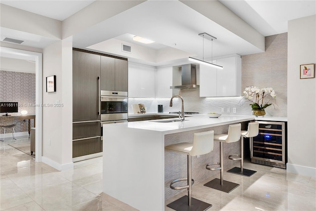 kitchen with wall chimney exhaust hood, modern cabinets, visible vents, and beverage cooler