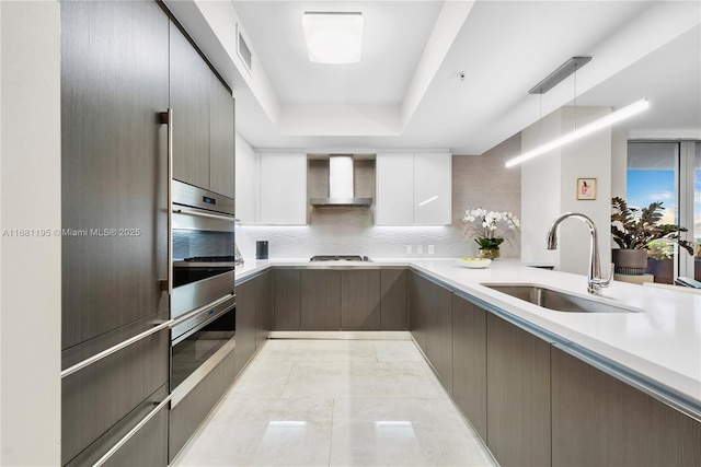 kitchen featuring oven, light countertops, wall chimney range hood, gas cooktop, and a sink