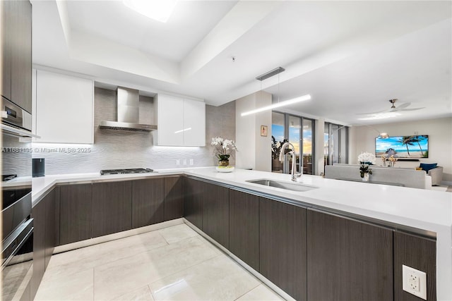 kitchen featuring gas cooktop, dark brown cabinetry, a sink, light countertops, and wall chimney range hood