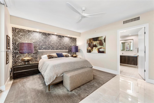 bedroom featuring visible vents, ensuite bathroom, an accent wall, baseboards, and wallpapered walls