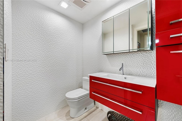 half bathroom featuring toilet, vanity, and a textured wall