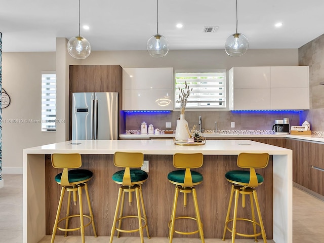 kitchen featuring stainless steel fridge, a breakfast bar, white cabinetry, and hanging light fixtures