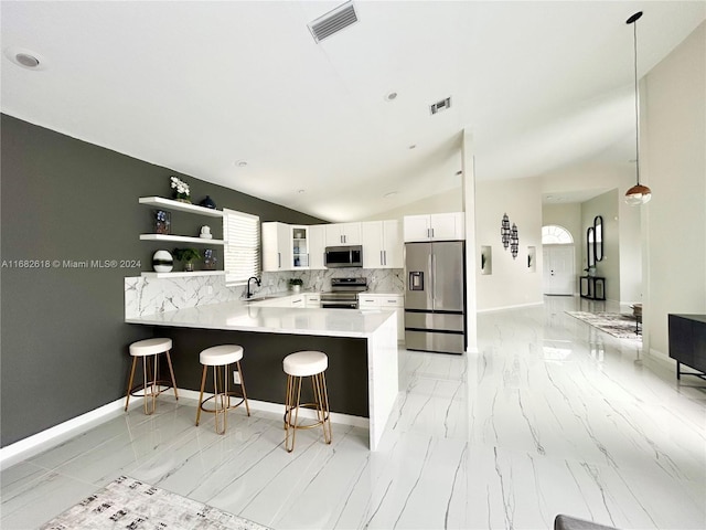 kitchen with kitchen peninsula, stainless steel appliances, pendant lighting, white cabinetry, and lofted ceiling