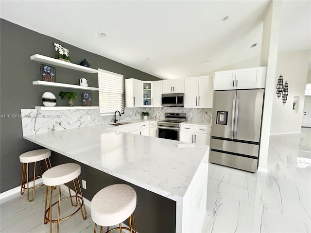 kitchen featuring sink, vaulted ceiling, a breakfast bar area, white cabinets, and appliances with stainless steel finishes