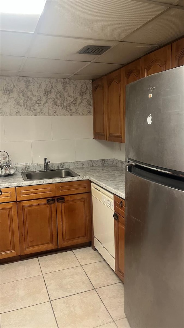 kitchen featuring dishwasher, sink, stainless steel fridge, a drop ceiling, and light tile patterned floors