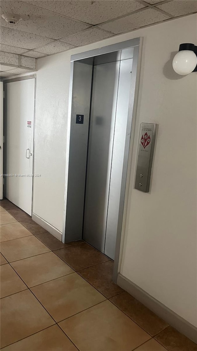 hall with a paneled ceiling, tile patterned floors, and elevator