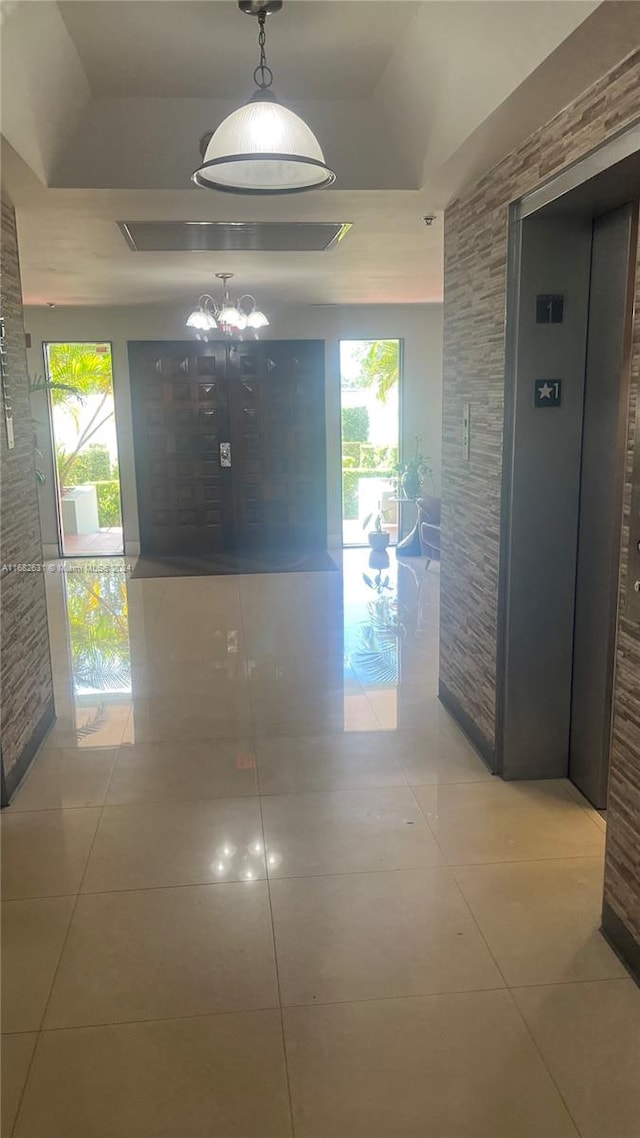 corridor with elevator, a tray ceiling, plenty of natural light, and light tile patterned floors