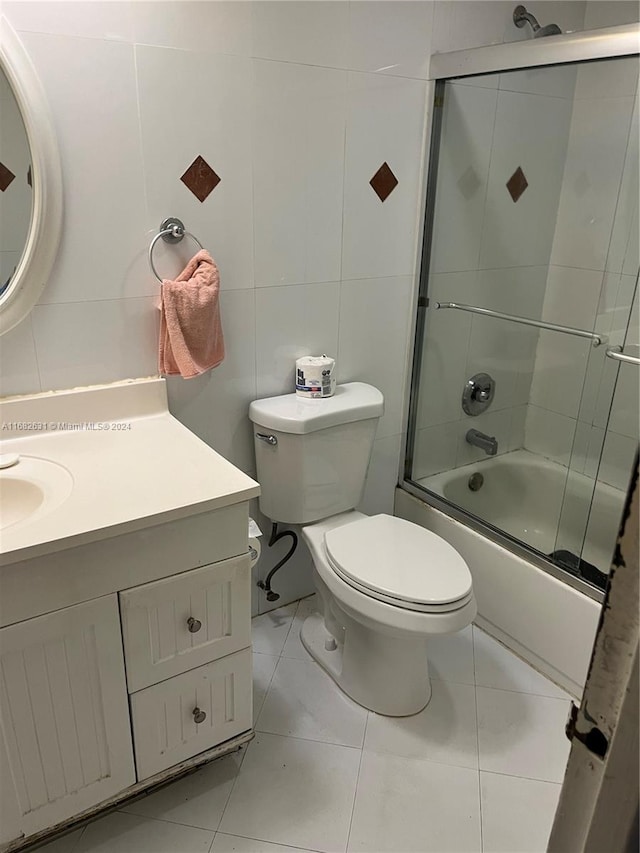 full bathroom with shower / bath combination with glass door, toilet, tile walls, vanity, and tile patterned flooring