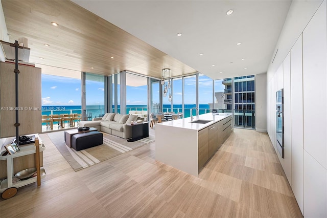 kitchen with white cabinets, an island with sink, expansive windows, sink, and a water view